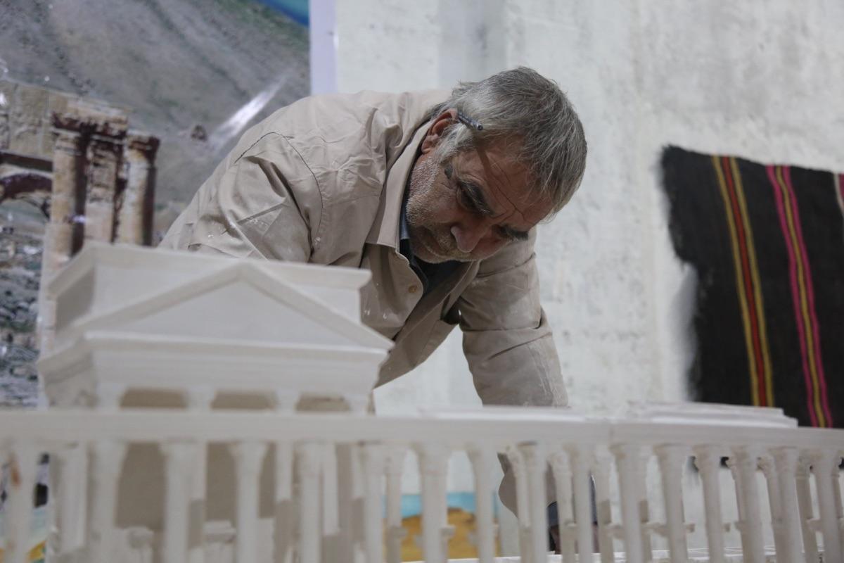 A man leans over a detailed white scale model of Palmyra's colonnade he is building.